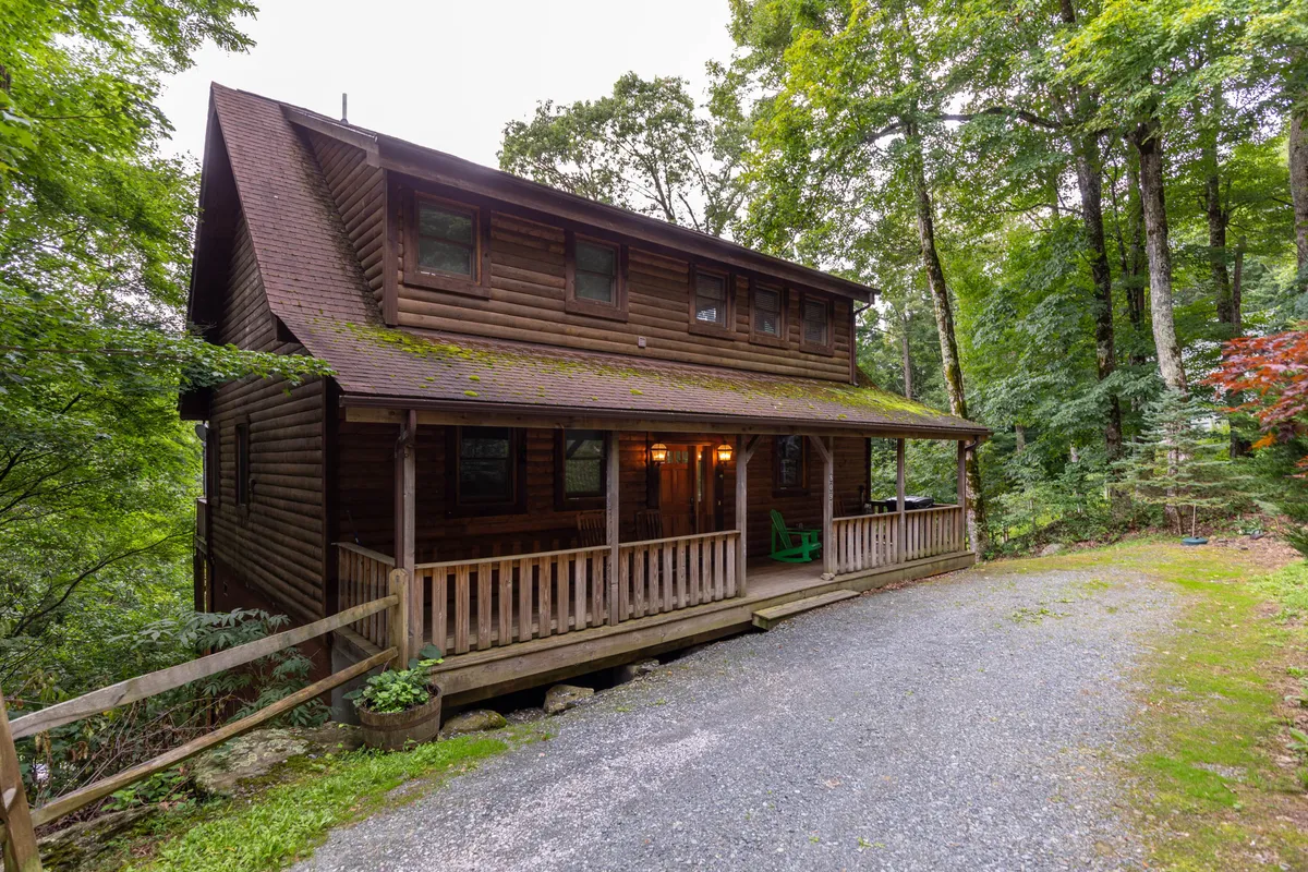 The hero image showcases the inviting wooden façade of the cabin, highlighted by a classic green rocking chair on the spacious front porch. Sunset light bathes the porch, hinting at the breathtaking mountain views guests can enjoy. The natural surroundings evoke a sense of tranquility and connection to nature, with the porch serving as the perfect spot for relaxation and taking in the scenery.