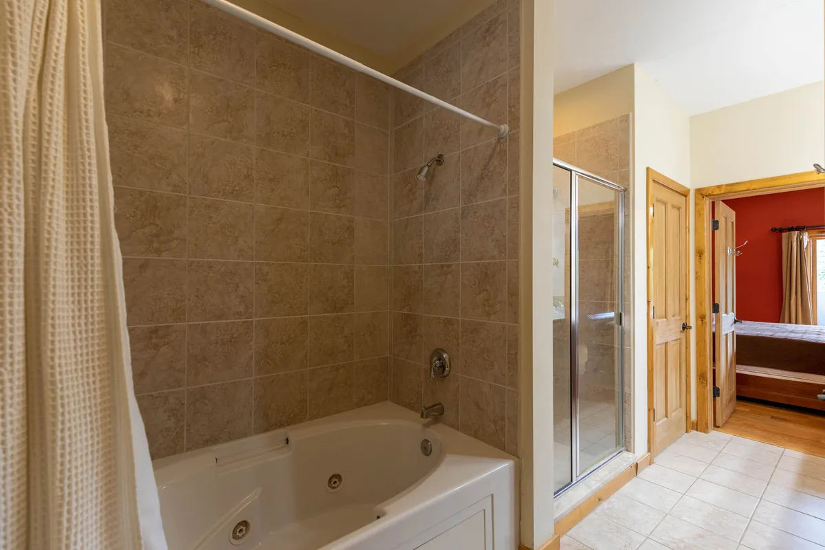A tranquil bathroom setting with a luxurious Jacuzzi tub and adjacent walk-in shower, filled with natural light. The spa-like ambiance is perfect for unwinding after a day in the mountains, emphasizing relaxation and self-care.