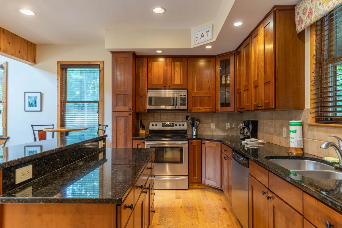 A close-up of the kitchen area showcases granite countertops, stainless steel appliances, warm wood cabinetry, and large windows that invite natural light and mountain views. The space is styled for both meal prep and socializing, highlighting the kitchen's role as a hub for shared experiences.