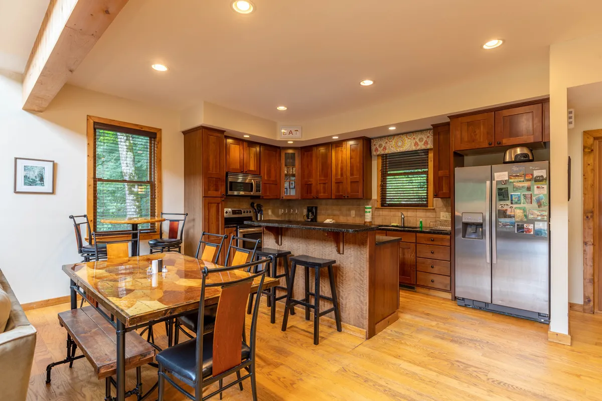 This image showcases the inviting kitchen and dining area, featuring wooden cabinets, a spacious table, and stainless steel appliances. Natural light streams in, highlighting a communal space ideal for gathering after a day outdoors.