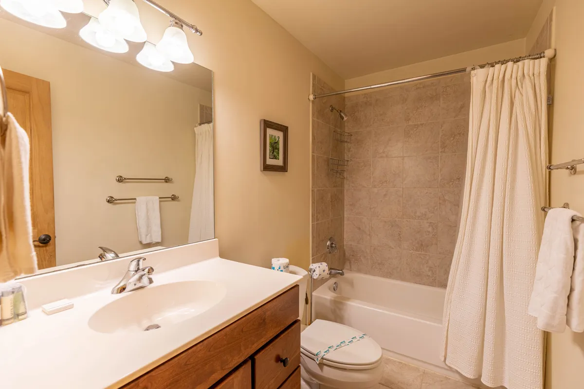 This image features a serene bathroom with a prominent bathtub, vanity, mirror, and towel rack. The space exudes calmness, ideal for indulging in self-care or sharing a relaxing soak after a day spent exploring picturesque mountain towns and hiking trails.
