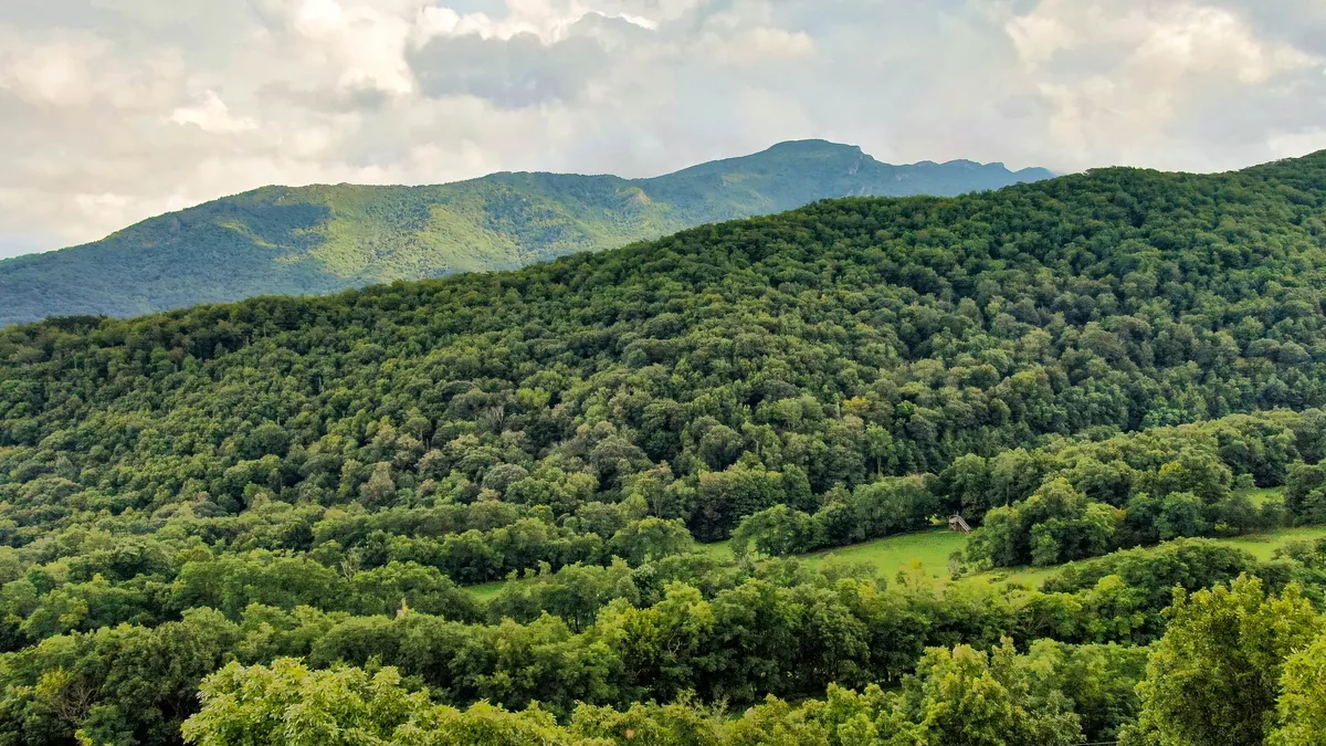 A sweeping vista of rolling green hills, distant mountains, and lush forest—a classic mountain landscape that sets the backdrop for every outdoor moment. The open sky and wide horizon invite thoughts of sunrise coffees and late-night stargazing.