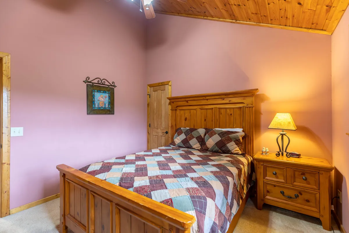 A warm, inviting bedroom with a wooden bed and colorful quilted bedspread, accented by a lamp and framed artwork. The window allows in natural light, enhancing the room’s cozy feel, ideal for quiet moments and shared stories.
